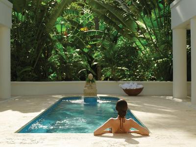 Ein Pool mit Person im Wasser, umgeben von Säulen und dichtem Grün.