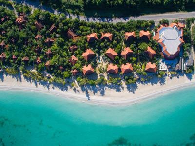 Luftaufnahme eines Resorts mit roten Dächern am weißen Sandstrand und türkisem Meer.