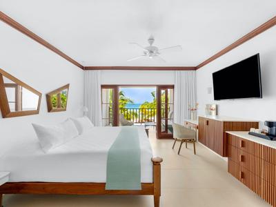 Bright hotel room with double bed, TV, balcony, and sea view.