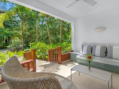 Offener Sitzbereich mit Sofa und Stühlen, Blick auf tropischen Garten mit Palmen.