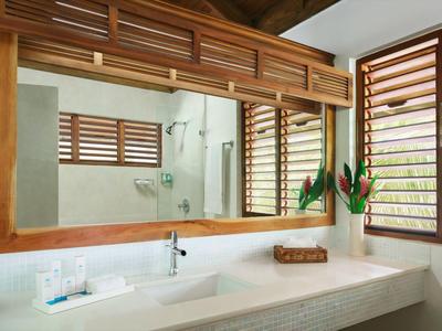 Modern hotel bathroom with large mirror, wooden frame, and decorative plants by the window.