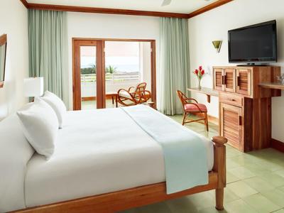 Helles Hotelzimmer mit großem Bett, Holzmöbeln und Balkon mit Blick ins Freie.