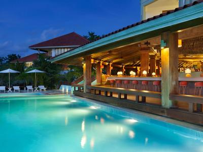 Ein beleuchteter Pool neben einer Bar im Freien in einem Hotel bei Abenddämmerung.