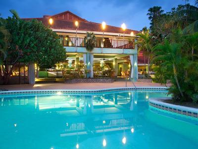 Evening view of a lit hotel with a large swimming pool and tropical plants.