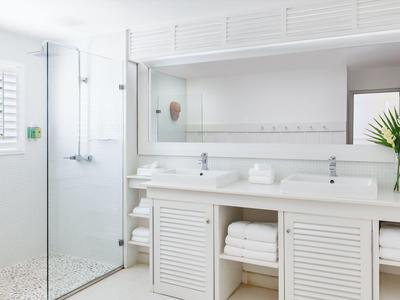 Helles Badezimmer mit großem Spiegel, Waschtischen und Duschecke in einem Hotelzimmer.