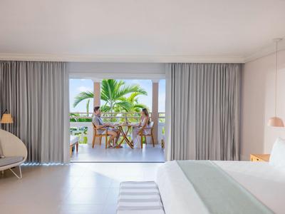 Modern eingerichtetes Hotelzimmer mit Blick auf Terrasse und tropische Pflanzen.