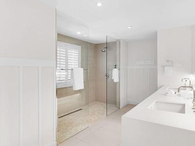 Helles, modernes Badezimmer mit Doppelwaschbecken, Glasduschkabine und Badewanne unter einem Fenster.