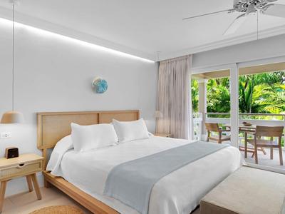 Geräumiges Hotelzimmer mit Doppelbett, Holzmöbeln und Blick auf eine grüne Terrasse.