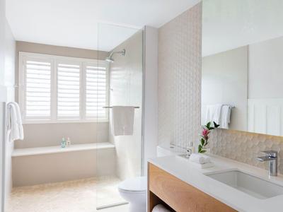 Helles Badezimmer mit Badewanne, Dusche, großem Spiegel und modernem Waschbecken.