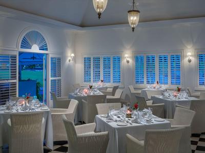 Elegantes Hotelrestaurant mit weißen Möbeln, gedeckten Tischen und Blick auf das Meer durch Fenster.
