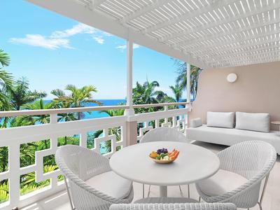Balkon mit Tisch, Stühlen und Sofa mit Meerblick und Palmen bei klarem Himmel.