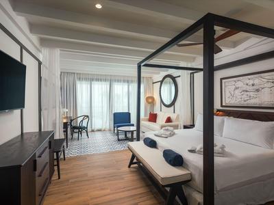 Helles Hotelzimmer mit Himmelbett, TV, Schreibtisch und Sitzbereich am Fenster.