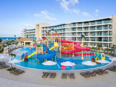 Bunte Wasserrutsche und Planschbecken vor einem Hotelgebäude mit Meerblick.
