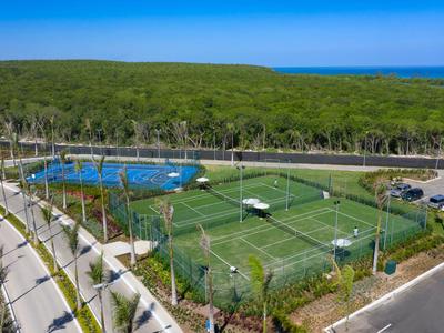 Blick auf Tennisplätze neben einem Pool und Parkplätzen in einer grünen Hotelanlage.