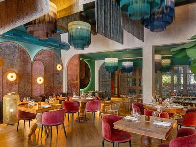 Elegantes Restaurant mit bunten Kronleuchtern, roten Sesseln und warmem Holzinterieur.