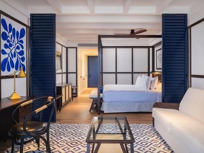 Modern eingerichtetes Hotelzimmer mit Doppelbett, Sofa und Schreibtisch in warmen Farbtönen.