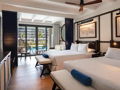 Helles Hotelzimmer mit zwei großen Betten, Balkon und Blick auf Palmen und Pool