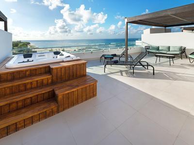 Terrasse mit Whirlwanne, Liegestühlen und Meerblick unter blauem Himmel.