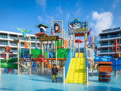 Bunter Wasserspielplatz mit Rutschen und Wasserattraktionen in einem Hotelresort bei blauem Himmel.