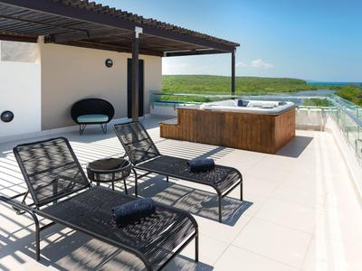 Dachterrasse mit zwei Liegestühlen, Whirlpool und Meerblick bei klarem Himmel.