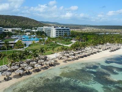 Strandresort mit Liegestühlen, Sonnenschirmen, Pool und umliegender Naturlandschaft.