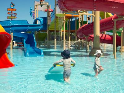 Kinder spielen im flachen Wasserbereich eines Wasserrutschenparks bei sonnigem Wetter.
