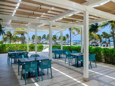 Überdachter Außenbereich eines Restaurants mit blauen Tischen und Stühlen und Blick auf Palmen und Meer.