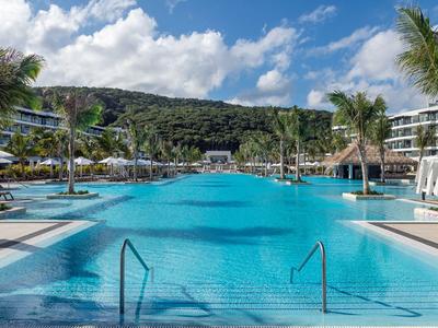 Großer Pool mit Blick auf bewaldete Hügel in einem modernen Hotelresort unter blauem Himmel.
