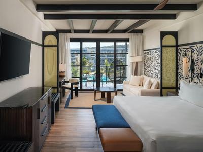 Modernes Hotelzimmer mit großem Bett, Sofa, TV und Balkon mit Blick auf die Stadt.