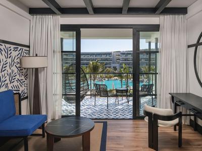 Modern eingerichtetes Hotelzimmer mit Blick auf einen Pool und Garten durch eine Glas-Schiebetür.