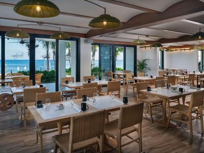 Helles, modernes Restaurant mit Holzmöbeln und Blick auf das Meer durch große Fenster.