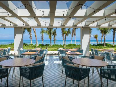 Offener Speiseraum mit Tischgruppen und Blick auf das Meer und Palmen