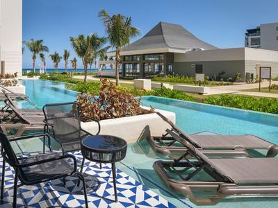 Moderner Hotelpool mit Liegestühlen, Stühlen und Tischen in tropischer Umgebung.