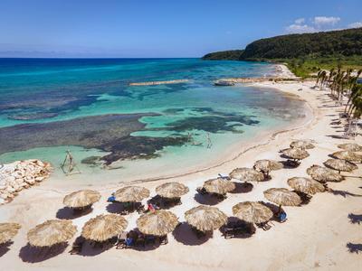 Strand mit klarem türkisfarbenem Wasser und Sonnenschirmen aus Stroh entlang des Sandes.