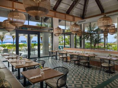 Modern restaurant with wooden roof, large windows, and view of a hotel pool area.