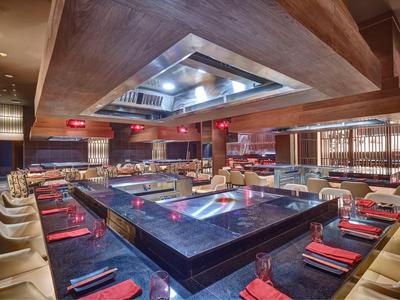 Modernes Restaurant mit quadratischem Grill in der Mitte und Sitzplätzen rundherum.