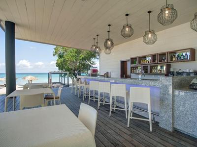 Moderner Hotelbarbereich mit weißem Mobiliar und Blick auf Meer und Strand.