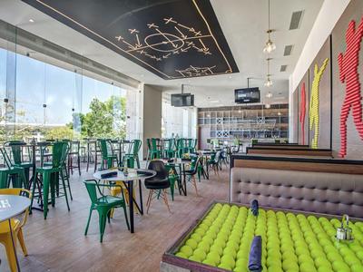 Modernes Hotelrestaurant mit großen Fenstern, grünen Stühlen und einer Tennisball-Dekoration.