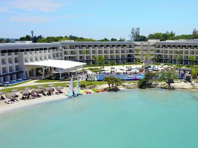 Moderner Hotelkomplex mit Pool und Strandbereich am klaren türkisfarbenen Wasser.