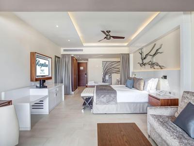 Helles Hotelzimmer mit Doppelbett, Sofa, TV und moderner Deckenbeleuchtung.