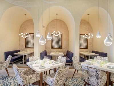 Modernes Hotelrestaurant mit bogenförmigen Nischen, dekorativen Stühlen und stilvollen Pendelleuchten.