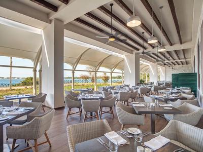 Modernes Hotelrestaurant mit Blick auf das Meer und eleganten weißen Stühlen.