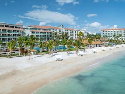 Großer Hotelkomplex am weißen Sandstrand mit Palmen und klarem blauem Wasser.