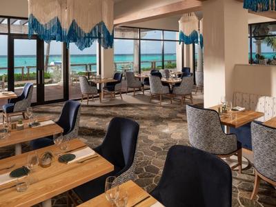 Moderner Hotelrestaurantbereich mit Holztischen, Stühlen und Meerblick durch große Fenster.