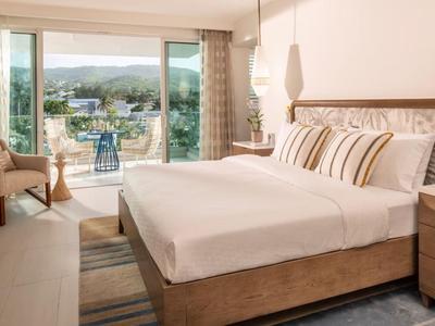 Modernes Hotelzimmer mit großem Bett und Balkon mit Aussicht auf Stadt und Berge.