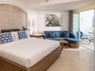 Modernes Hotelzimmer mit großem Bett, blauem Sofa und Balkon mit Meerblick.