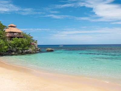 Strand met helder turquoise water, zand en hutten aan de rand van het bos onder een blauwe lucht.