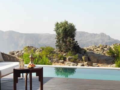 Moderne Terrasse mit Pool, Stuhl und Tisch mit Getränken vor Berglandschaft.