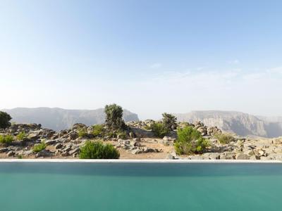 Blick auf eine felsige Landschaft mit vereinzeltem Grün hinter einem blauen Schwimmbecken