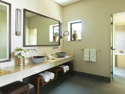Modern bathroom with double sinks, large mirror, towels, and open doorway to a bathtub area.